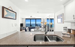 A modern kitchen with a large window, a dining area, and a view of the ocean.