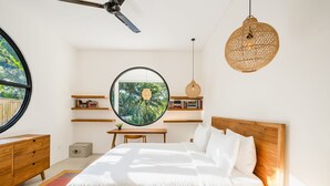 Une chambre à coucher comprenant un lit, un miroir rond, un ventilateur de plafond, une tête de lit en bois, une table de chevet et une bibliothèque.