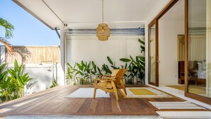 Une terrasse en bois avec une chaise, un luminaire suspendu et une porte-fenêtre coulissante donnant sur une pièce.