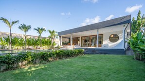 Une maison moderne dotée d’un grand patio, d’une piscine et d’une végétation luxuriante.