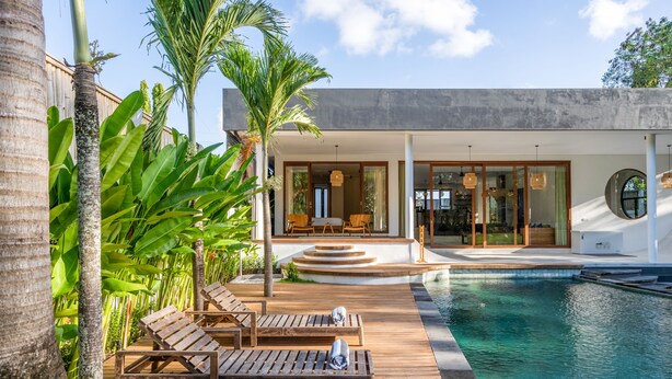 Une maison moderne dotée d’une piscine, d’une terrasse en bois et de plantes tropicales.