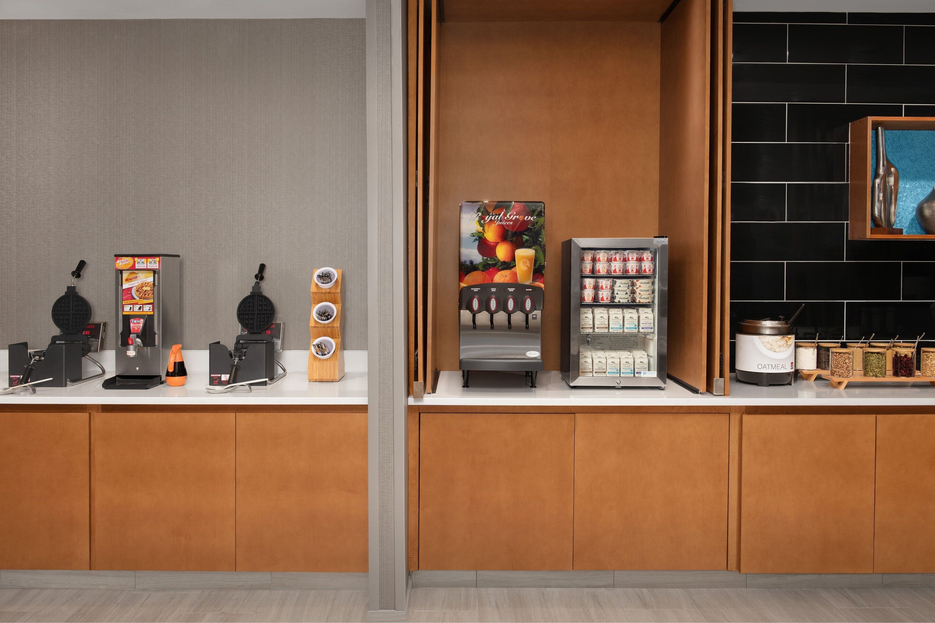 Et tekøkken med kaffemaskine, te-dispenser, frugt-dispenser, køleskab og en hylde med krydderier.