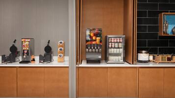 Et tekøkken med kaffemaskine, te-dispenser, frugt-dispenser, køleskab og en hylde med krydderier.
