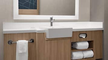 Un baño moderno con un lavamanos blanco, tocador de madera y un espejo sobre el lavamanos.