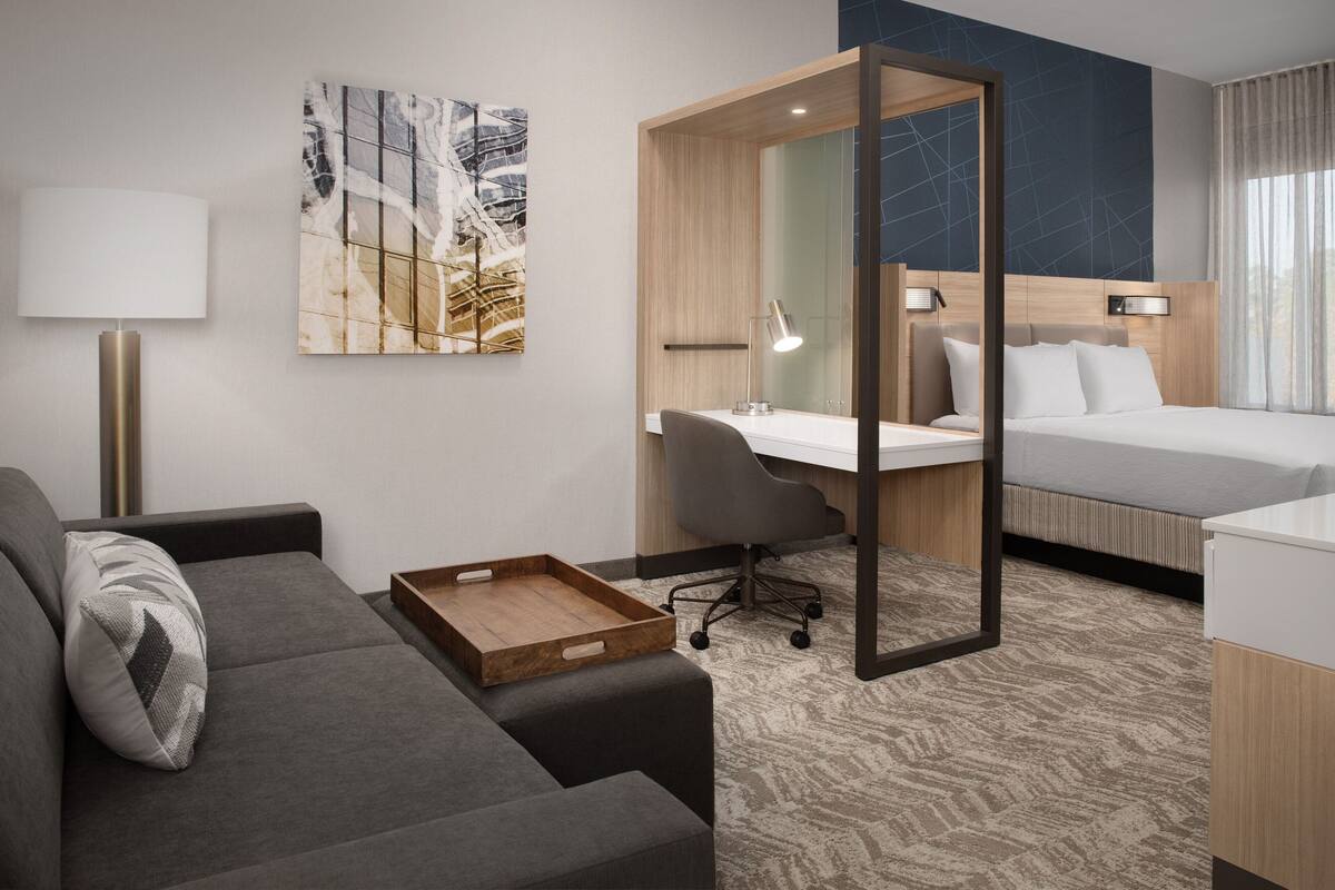 Een moderne hotelkamer met een bank, een bureau, een bed en een grote spiegel.