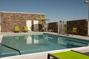A swimming pool with green chairs and a table, surrounded by a stone wall and a white fence. - Springhill Suites By Marriott Fayetteville I 95 (Fayetteville)