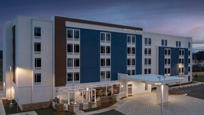 Een modern hotel met een blauw-witte gevel, meerdere ramen en een overdekt terras met zitplaatsen.