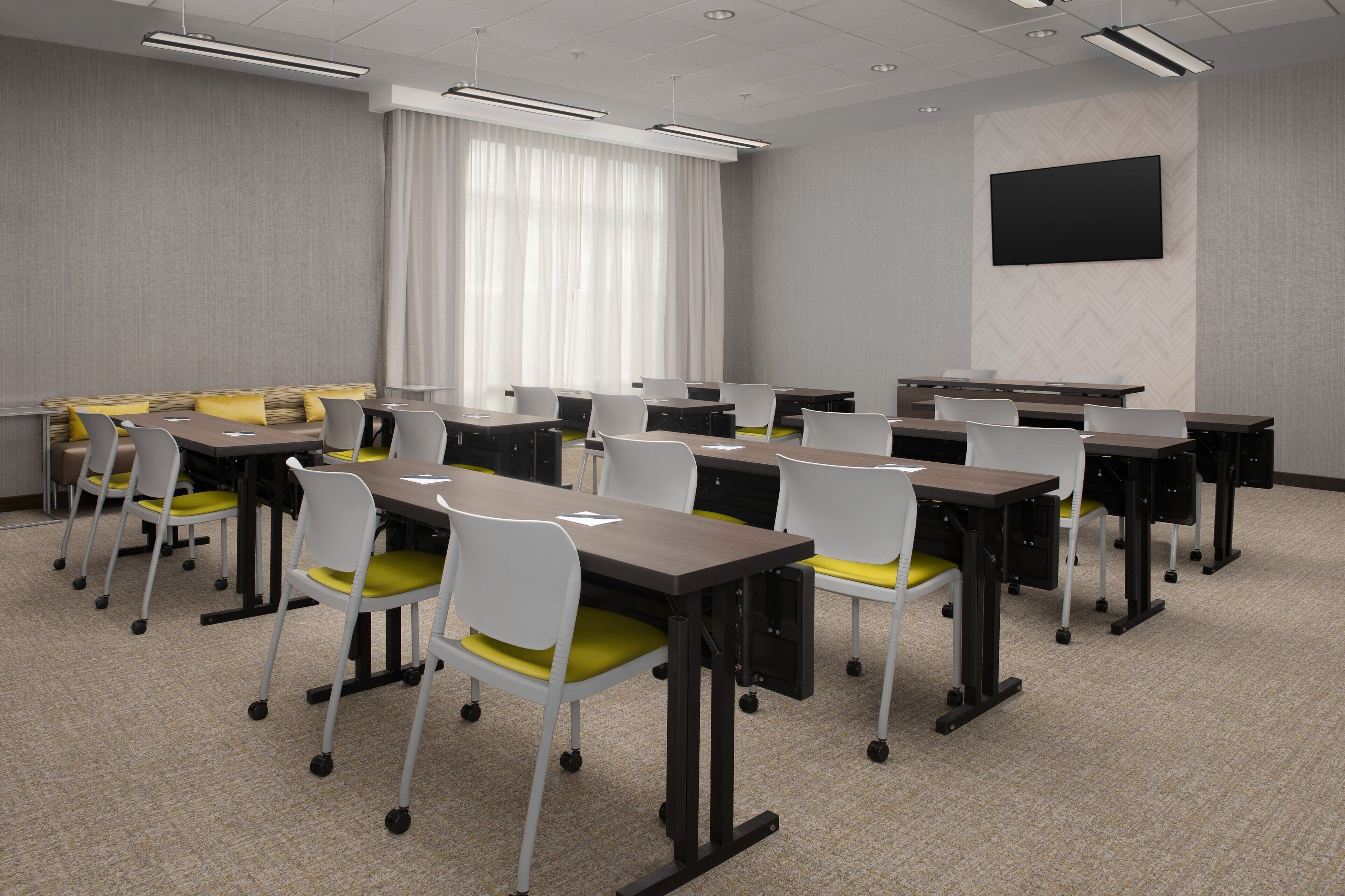 A conference room with tables and chairs, a large screen, and a window with curtains.