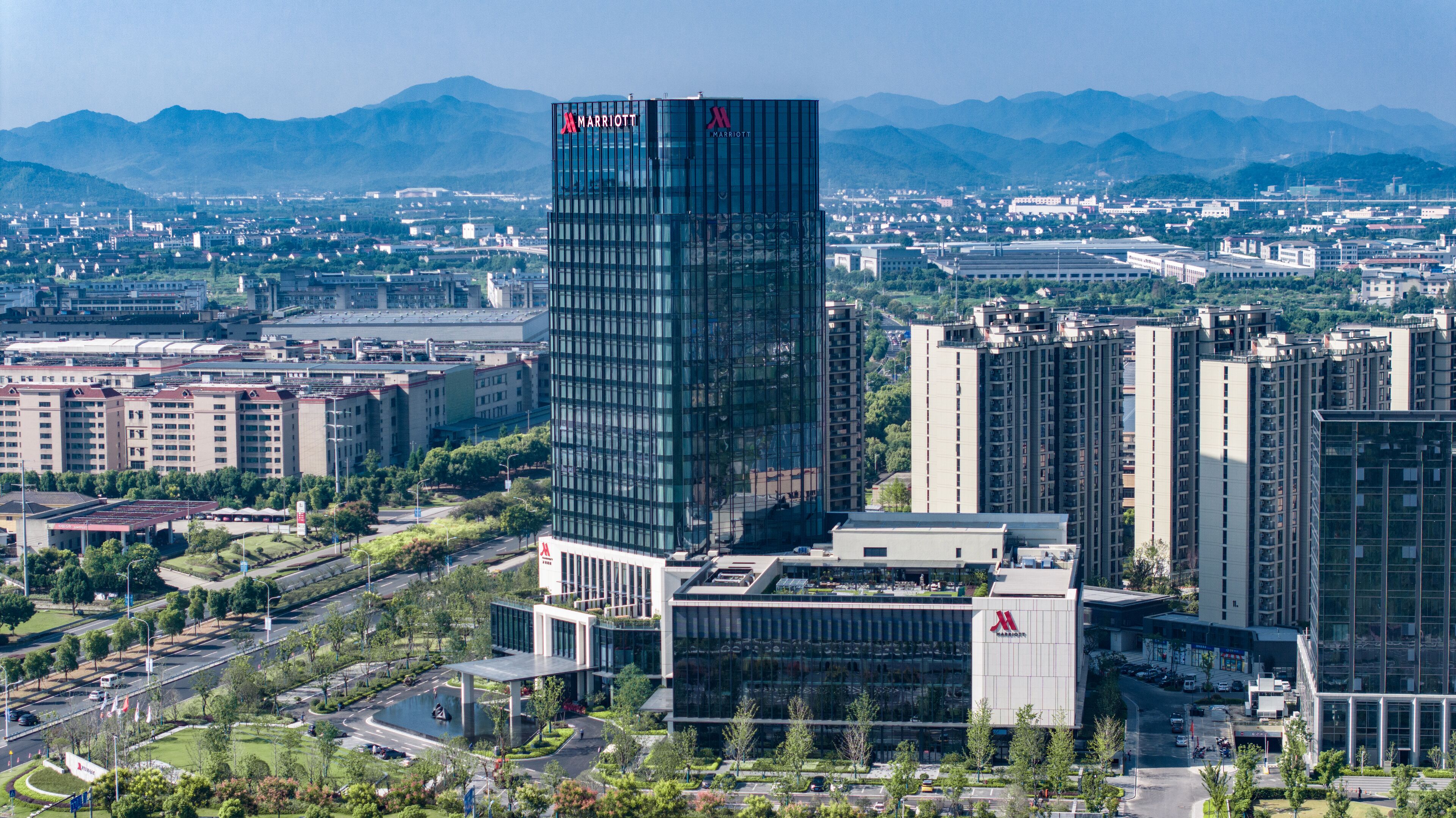 Un hotel moderno con un logotipo destacado de Marriott, rodeado de edificios urbanos y vegetación.