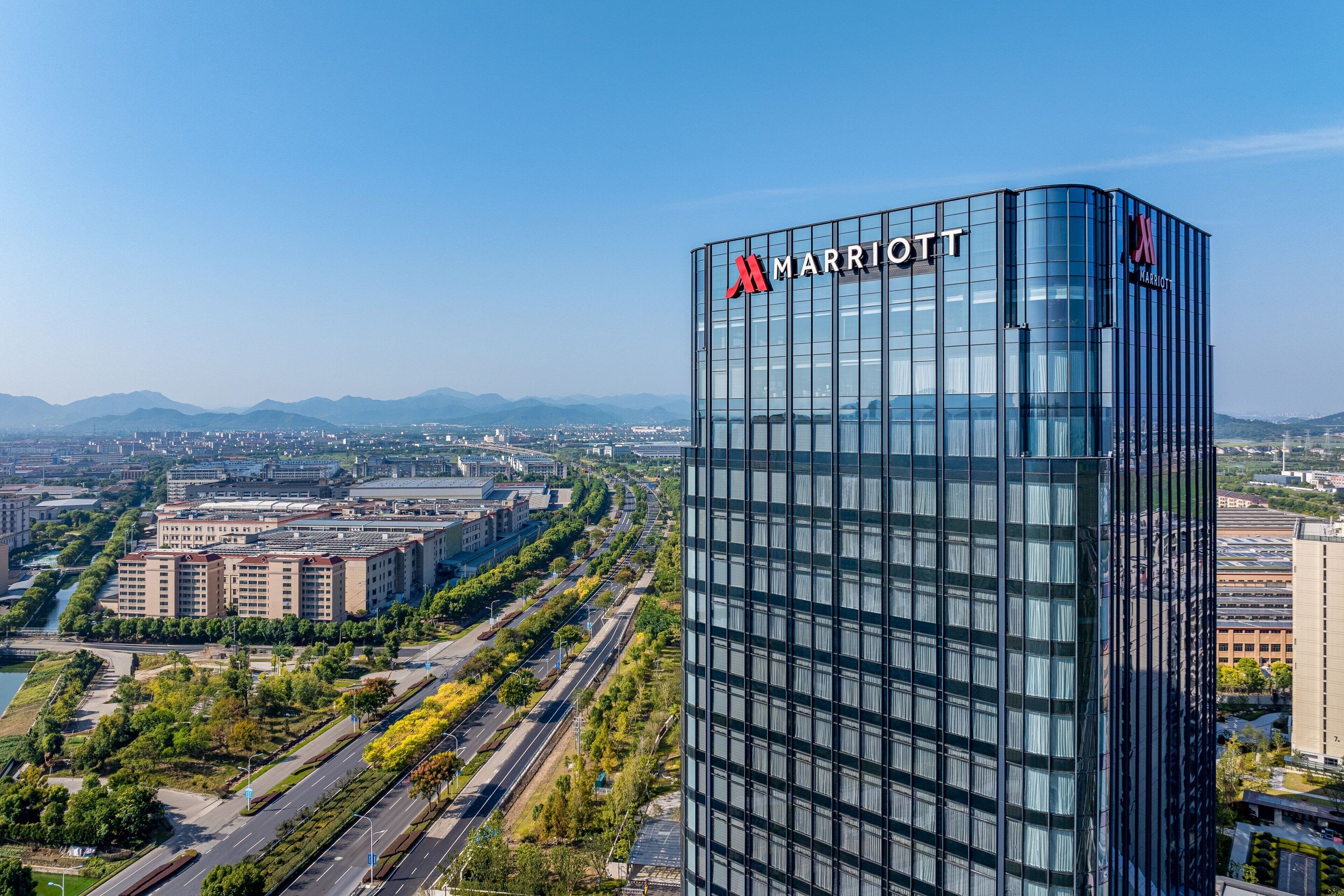 Ein modernes Marriott Hotel mit Glasfassade, umgeben von einer gepflegten Stadtlandschaft und fernen Bergen.