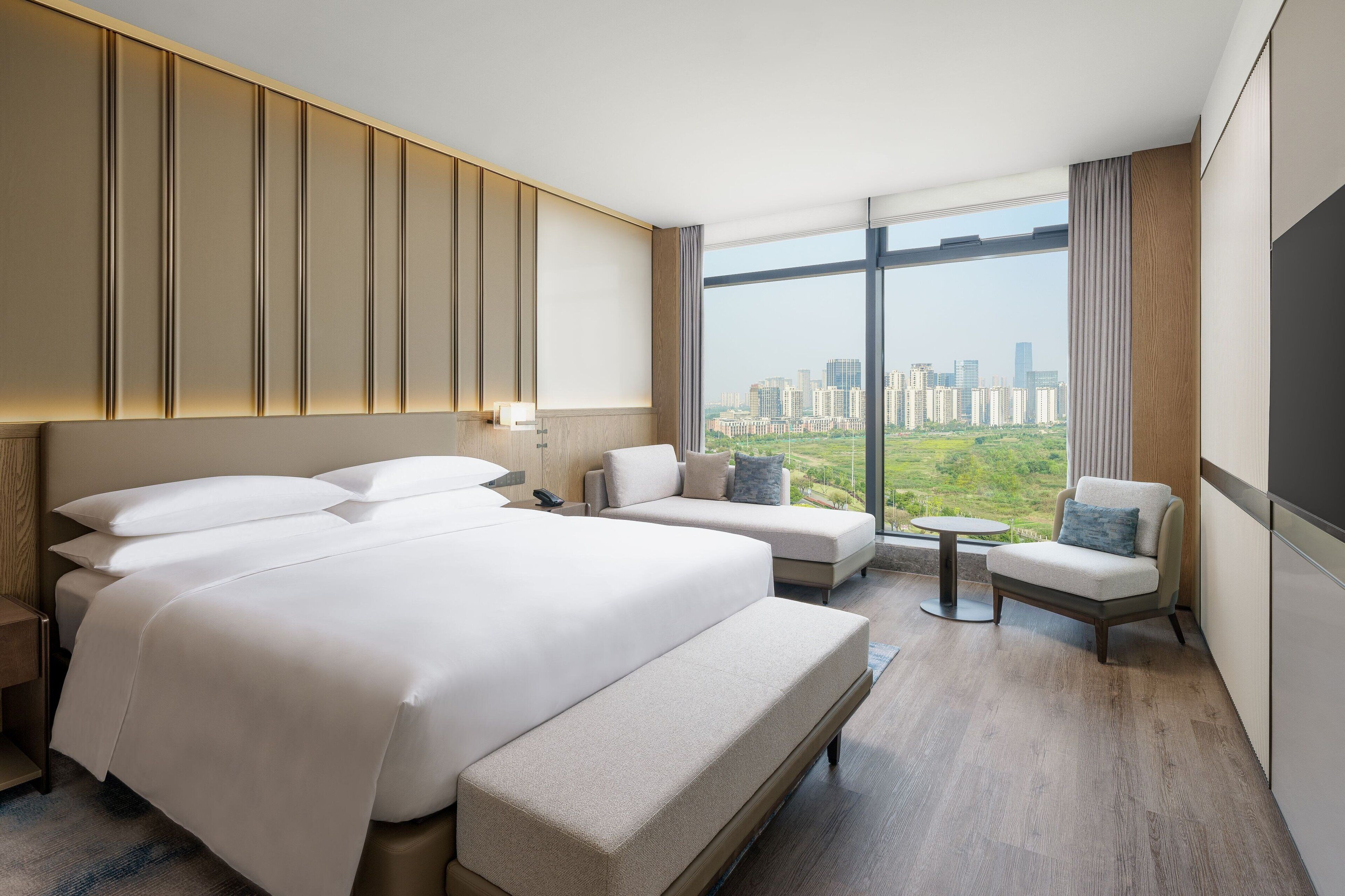 A modern hotel room with a large bed, two sofas, a small table, and a city view.