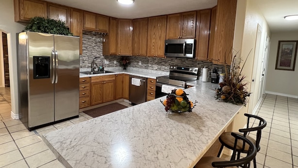 Una cocina moderna con armarios de madera, electrodomésticos de acero inoxidable, encimera de mármol y un frutero.