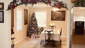 Un comedor con un árbol de Navidad, una mesa con sillas y un refrigerador.