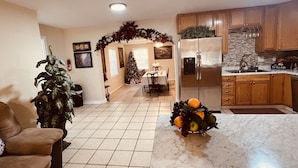 Un salón espacioso con una planta grande, un comedor con un árbol de Navidad y una cocina con un refrigerador de acero inoxidable y armarios de madera.