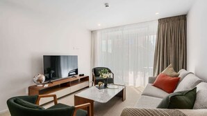 Ein modernes Wohnzimmer mit Flachbildfernseher, einer Couch, einem Couchtisch und einem Sessel.