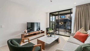Ein modernes Wohnzimmer mit Flachbildfernseher, Couchtisch, Sofa und einem Balkon mit Gartenmöbeln.