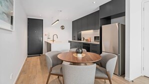 Een moderne keuken met donkere kastjes, een roestvrijstalen koelkast en een ronde houten eettafel met grijs gestoffeerde stoelen.