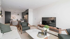Een moderne woonkamer met een bank, salontafel, televisie en een eethoek met stoelen en een tafel.