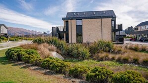 Een modern gebouw met twee verdiepingen, een plat dak, grote ramen en een aangelegde tuin met verschillende struiken en grassen.