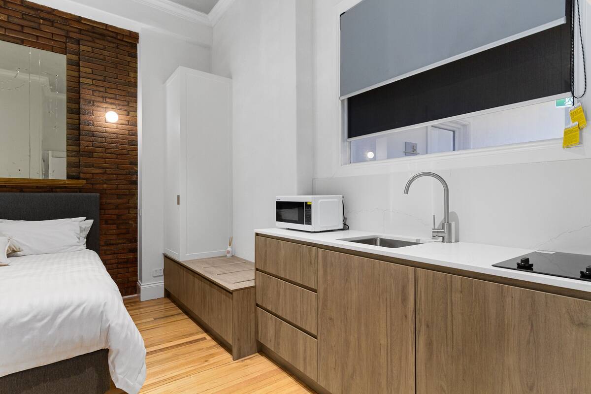 A compact bedroom with a bed, a small kitchenette, and a bathroom.