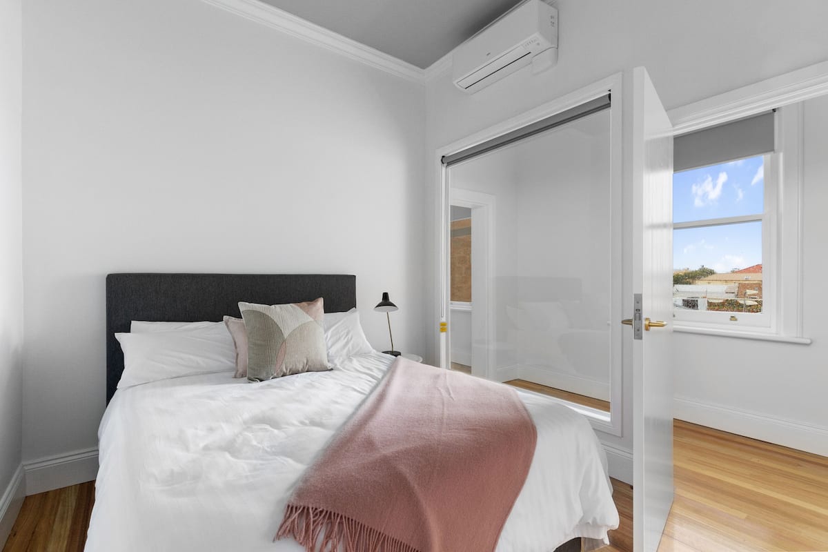 A bedroom with a bed, a nightstand, a window with a view, and a door leading to another room.