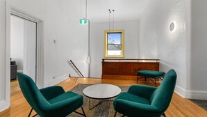 Ein modernes Zimmer mit zwei grünen Sesseln, einem runden Tisch, einer hölzernen Bank und Blick zum Himmel durch ein Fenster.