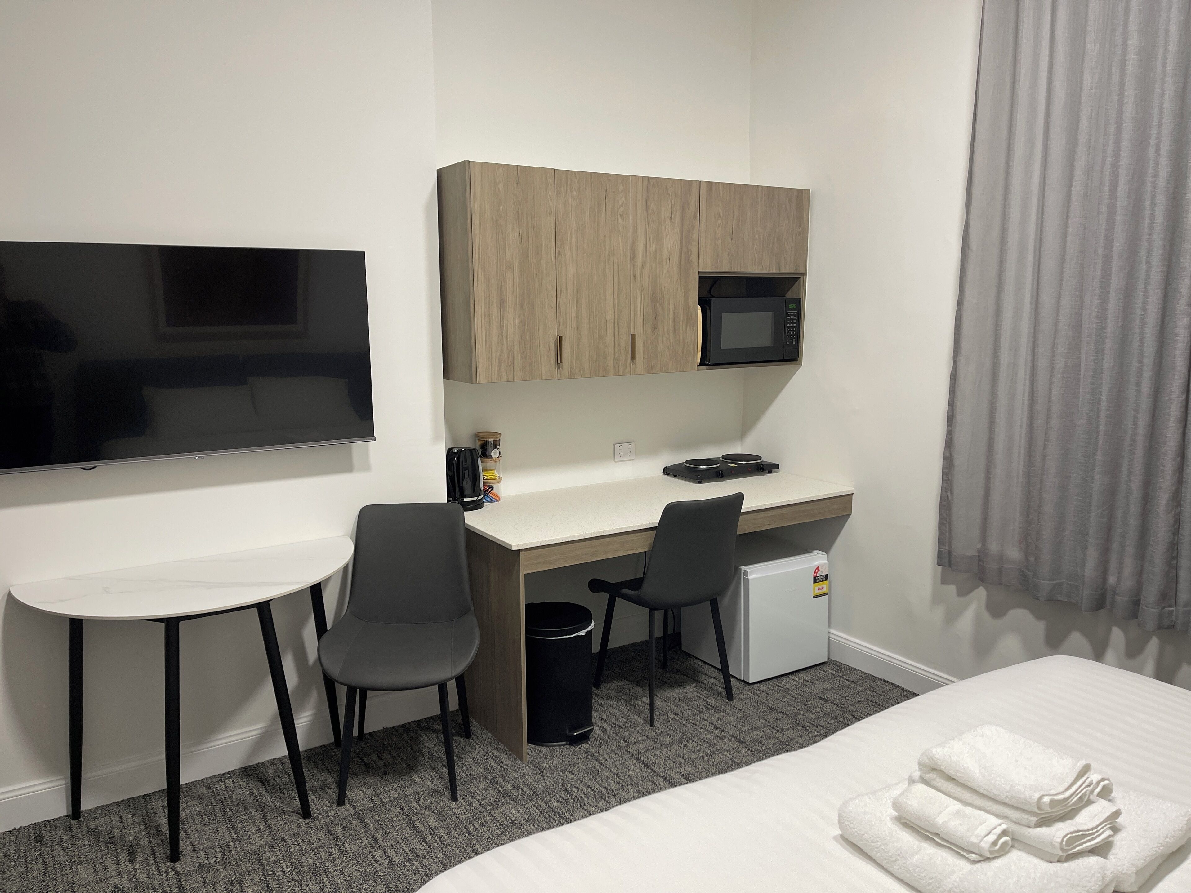 A hotel room with a bed, a desk with a computer, a TV, a microwave, and a small refrigerator.