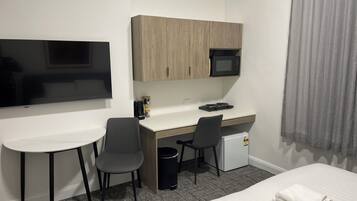 A hotel room with a bed, a desk with a computer, a TV, a microwave, and a small refrigerator.