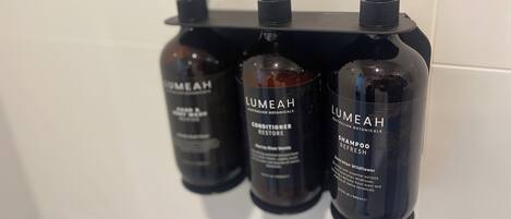 Tres botellas de acondicionador Lumeah sobre un dispensador negro con bomba.