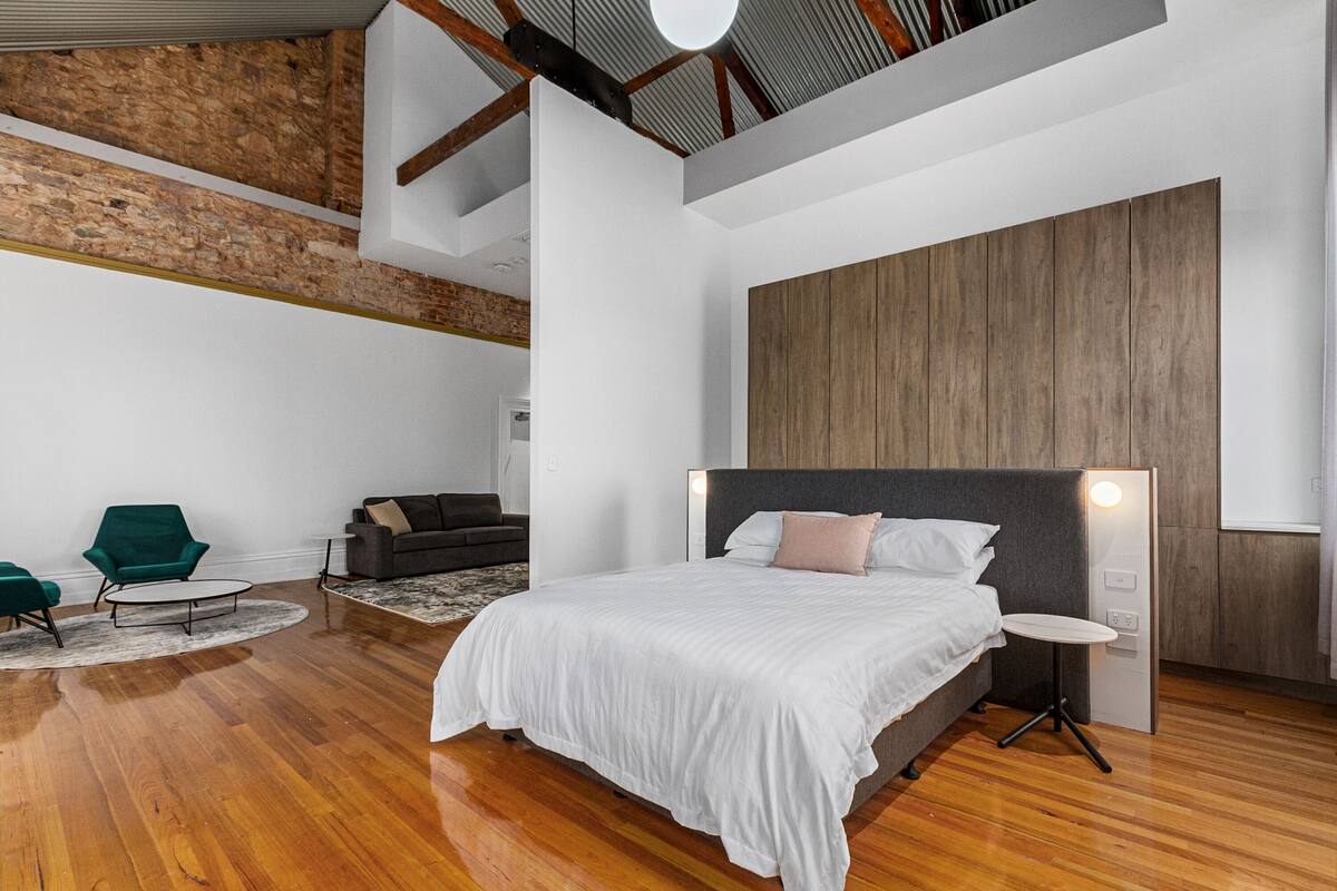 A modern bedroom with a large bed, a small round table, and a green armchair.