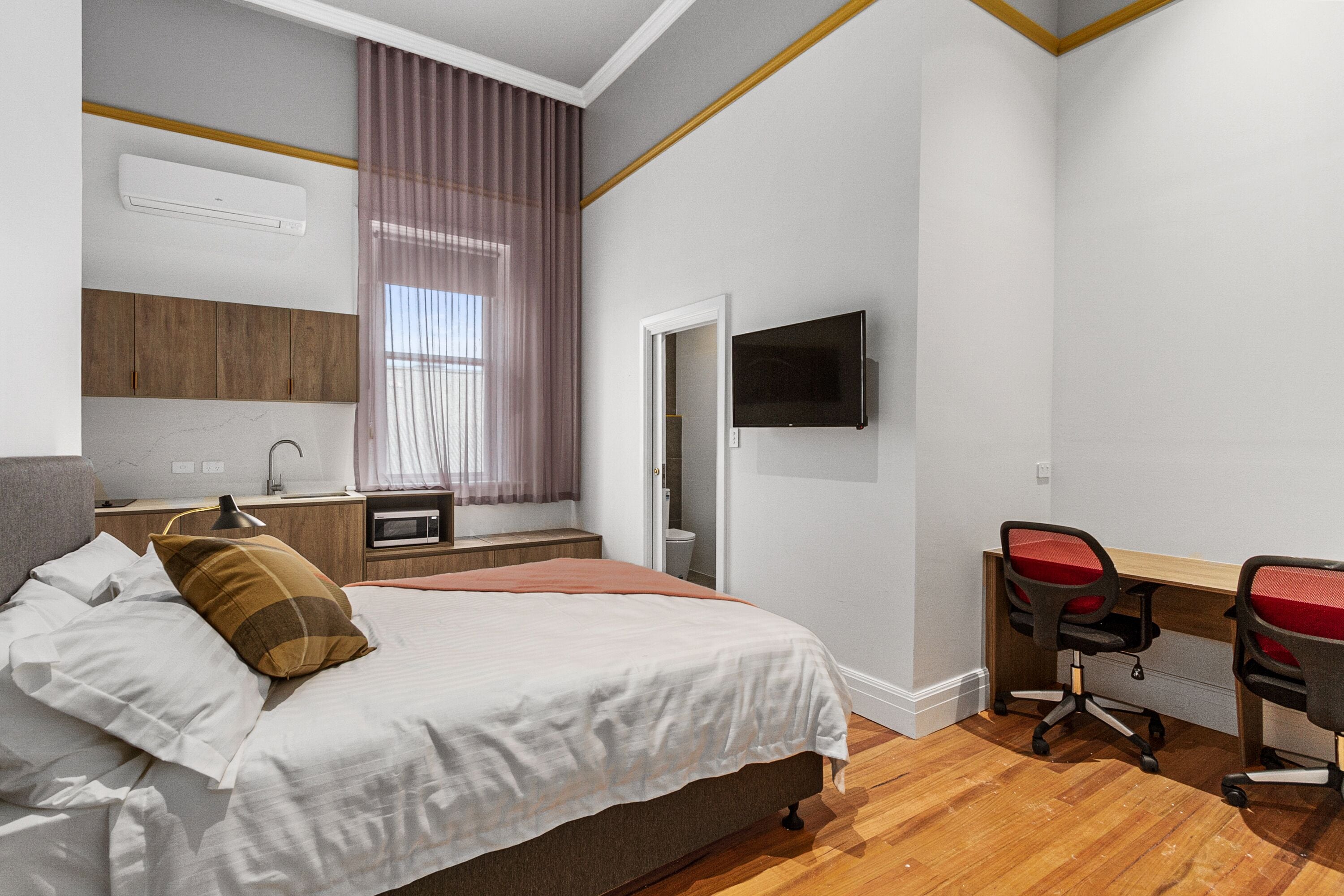 Un dormitorio con cama, mesita de noche, lámpara, televisor y un escritorio con dos sillas.