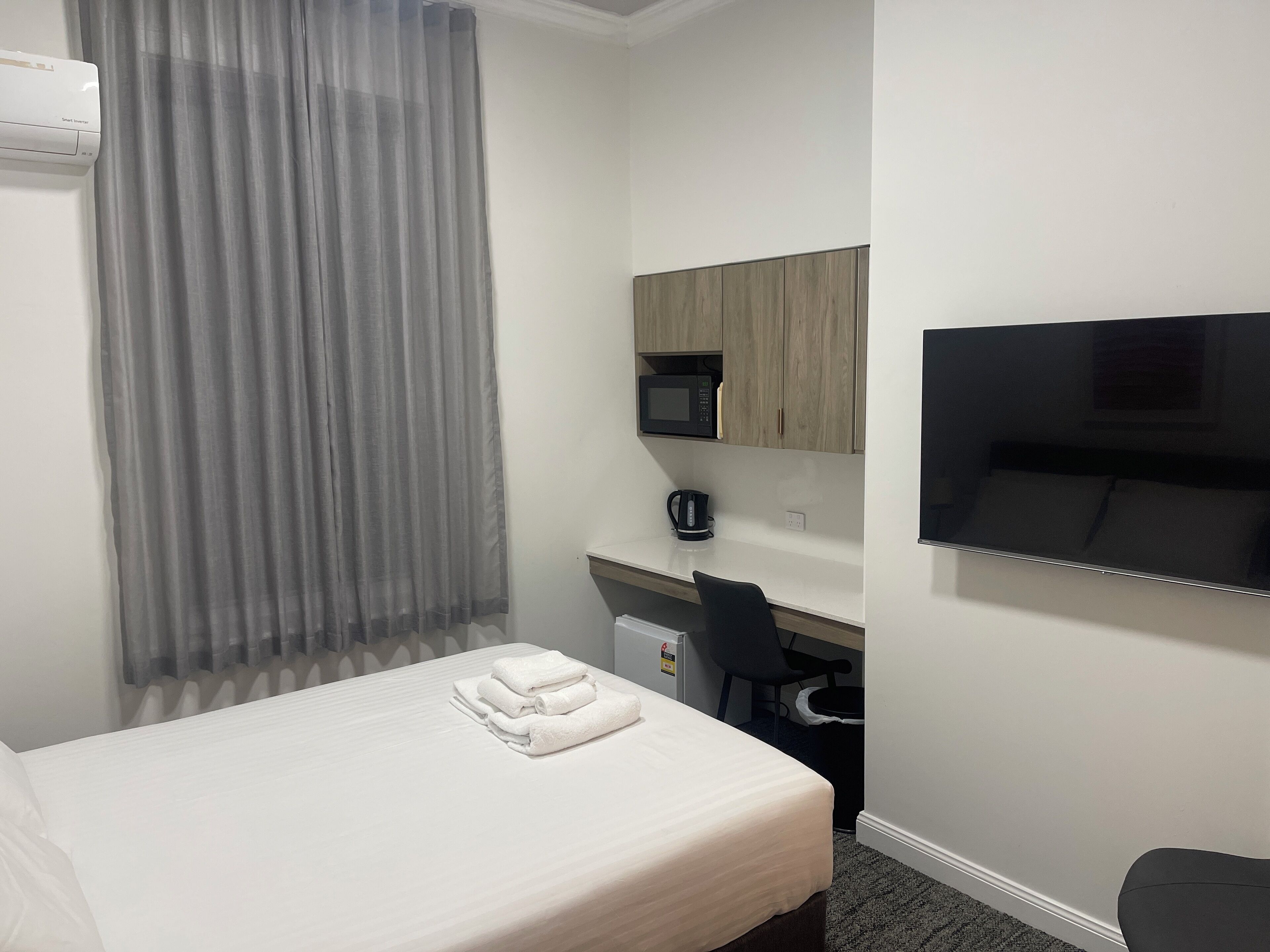 A hotel room with a bed, a desk with a chair, a microwave, a TV, and a window with curtains.