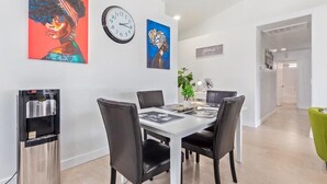 Uma área de jantar moderna com uma mesa branca, cadeiras pretas e um dispensador de água.