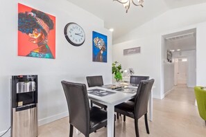 A modern dining area with a white table, black chairs, and a water dispenser. - 4BR Furnished Phoenix Home for Extended Stays (Phoenix)