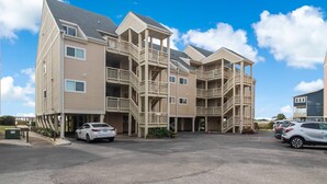 A multi-story hotel with balconies, a parking lot, and a clear blue sky. - Spectacular Ocean Views and Steps from the Beach (Oak Island)