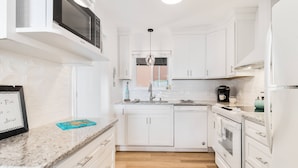 A modern kitchen with white cabinetry, a built-in microwave, a window, and a countertop with a framed picture. - Spectacular Ocean Views and Steps from the Beach (Oak Island)