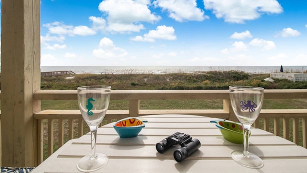 A table with two wine glasses, a bowl, and binoculars on a balcony overlooking a beach. - Spectacular Ocean Views and Steps from the Beach (Oak Island)