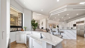 Una cocina moderna con una isla de mármol, armarios blancos y un ventanal grande.