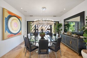 A modern dining room with a glass table, black chairs, a chandelier, and a large abstract painting.
