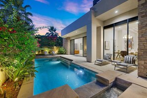 A modern pool area with a clear pool, lounge chairs, and a stone wall.