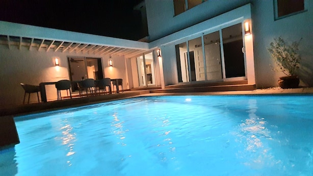 Une piscine dotée d’un patio couvert, d’un éclairage extérieur et de plantes en pot.