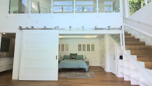 Un intérieur moderne avec un lit central, un escalier et une rambarde en verre.