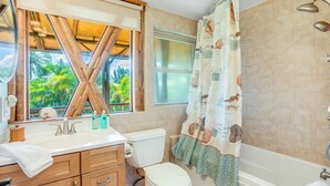 A bathroom with a wooden vanity, a toilet, a bathtub, and a shower curtain with a nautical theme. - The Iconic Bamboo House (Hanalei)