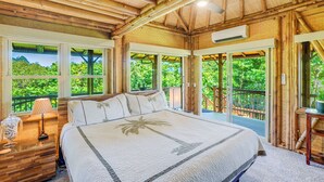 A spacious bedroom with a large bed, multiple windows, and a view of lush greenery. - The Iconic Bamboo House (Hanalei)