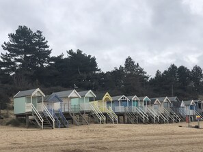 En række strandhytter med trætrapper, foran et baggrund af træer og en overskyet himmel.