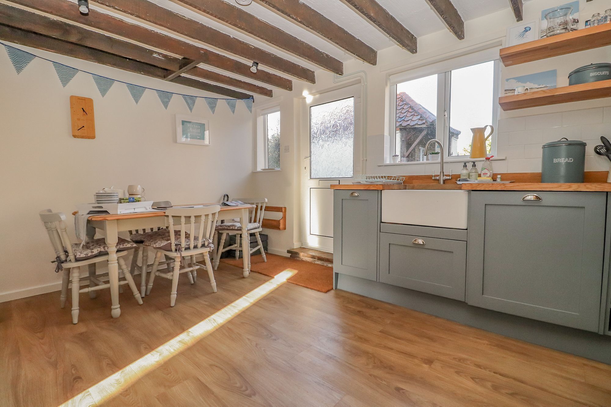 A kitchen with wooden flooring, a dining table with chairs, and grey cabinets.