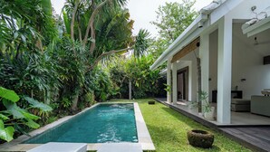 A swimming pool with two lounge chairs, surrounded by lush greenery and a modern house with a covered patio. - The Saya House Villa by Betterplace (Kerobokan)