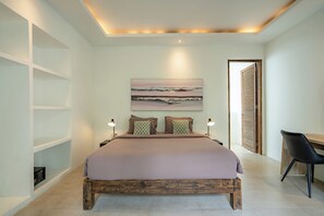 Quarto moderno com uma cama grande, abajures, uma escrivaninha e vista para a praia pela janela.