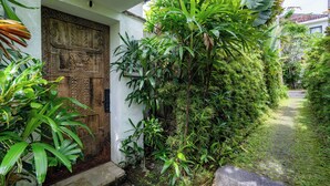 A traditional wooden door with intricate carvings, surrounded by lush green plants and a stone pathway leading to a house. - The Saya House Villa by Betterplace (Kerobokan)