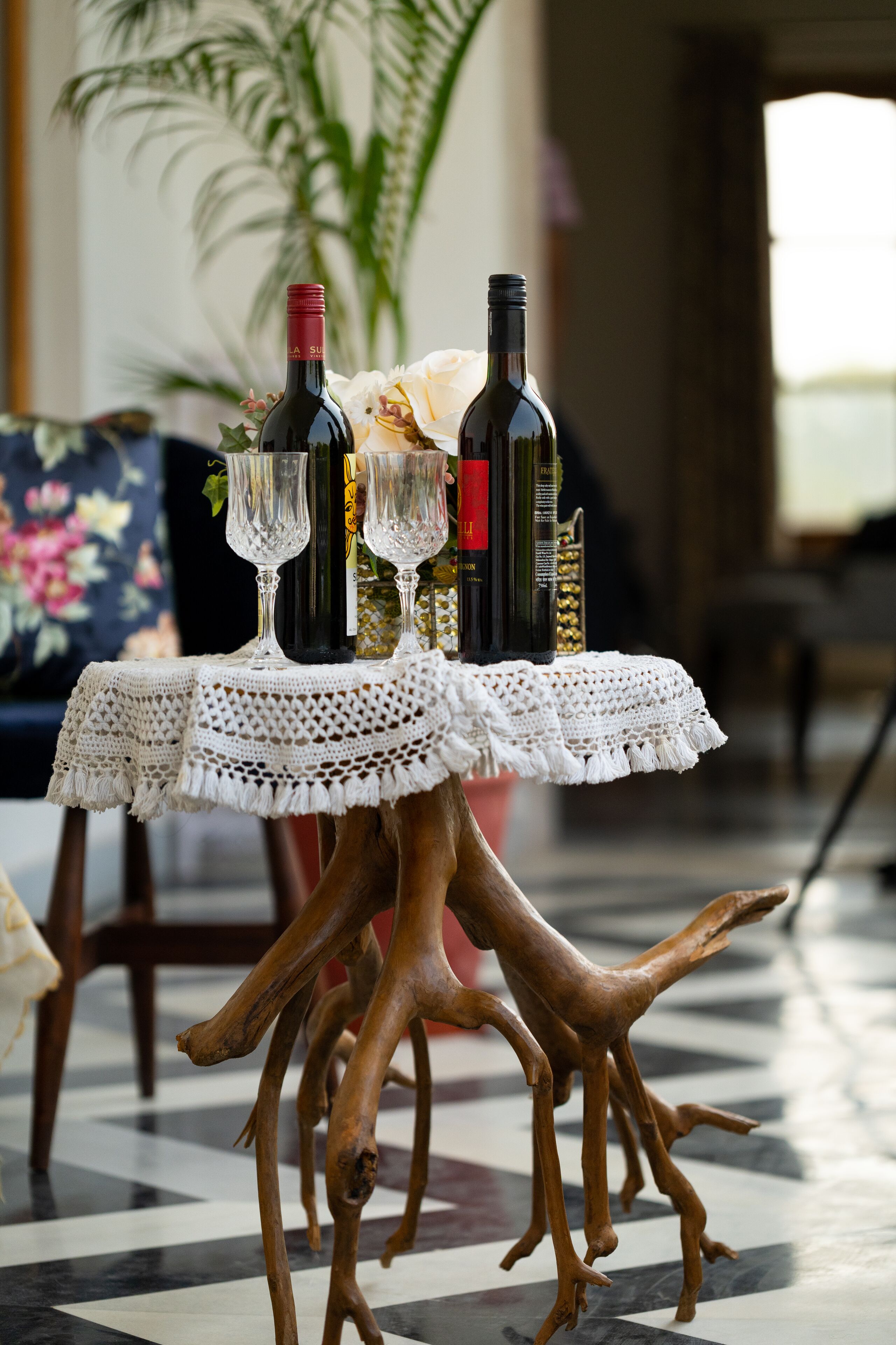 A table with wine bottles and glasses, set on a wooden stand with a checkered floor.
